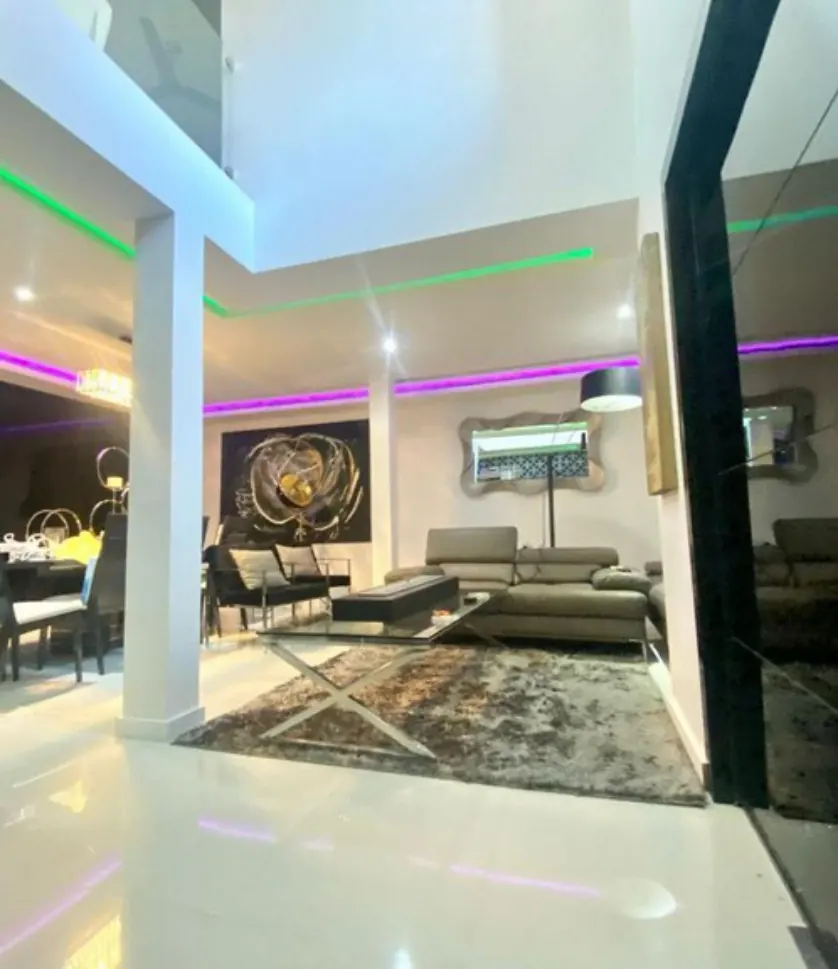 Sala residencial de doble altura con tiras LED verdes y moradas integradas en plafones