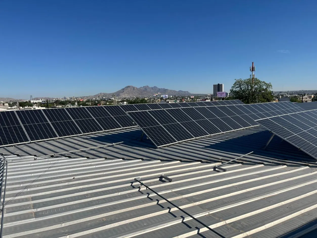 Hileras de paneles solares sobre techo de lámina con la ciudad y montañas al fondo